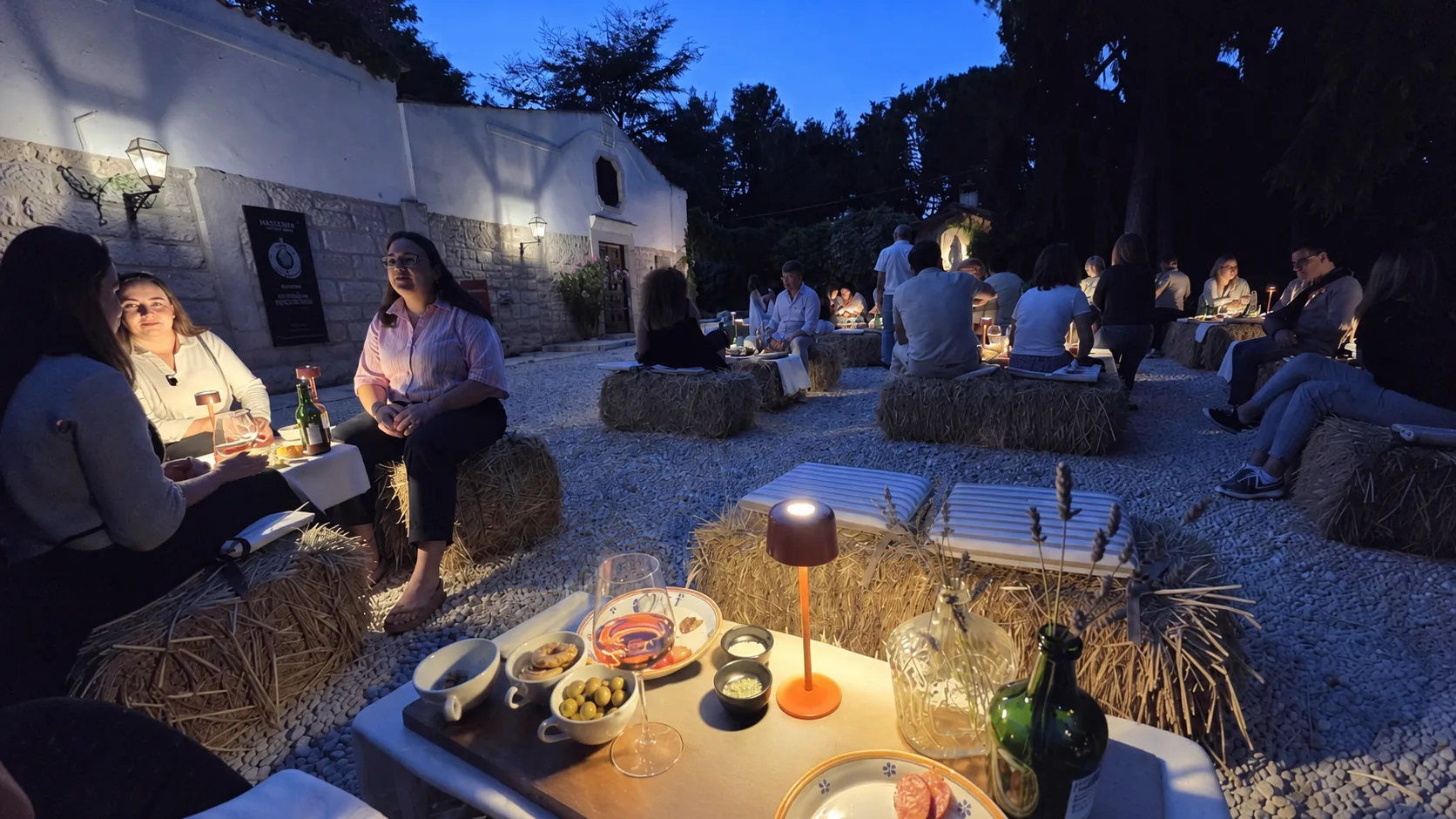 La serata dei laboratori: tavoli con lanterne e sedute in balle di fieno al crepuscolo